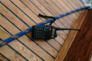 A two-way radio placed on a wooden surface next to a blue rope, possibly on a boat deck.